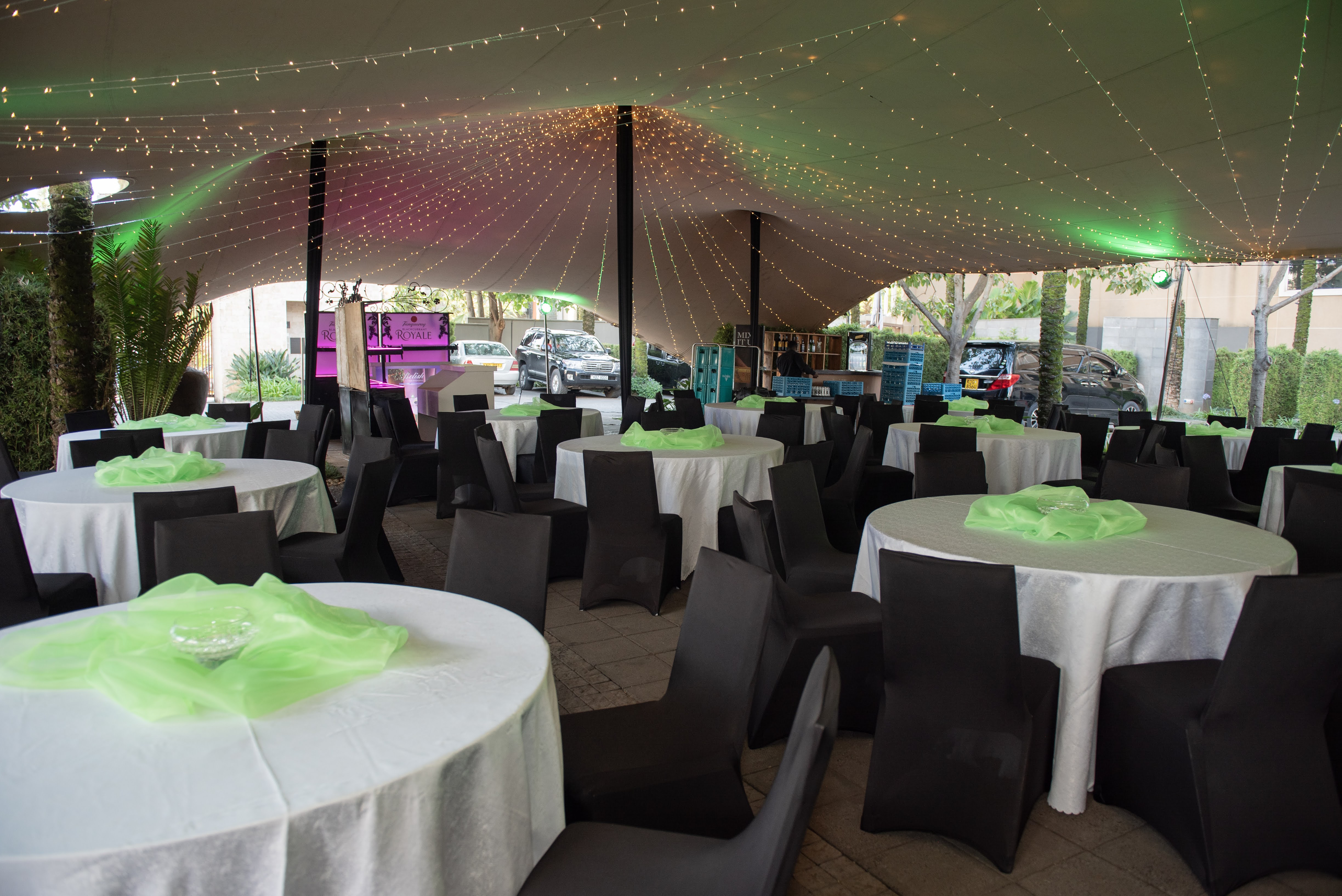 A row of gold-framed cream armchairs with branded plinths beneath fairy-lit tent drapery — a polished corporate setup
