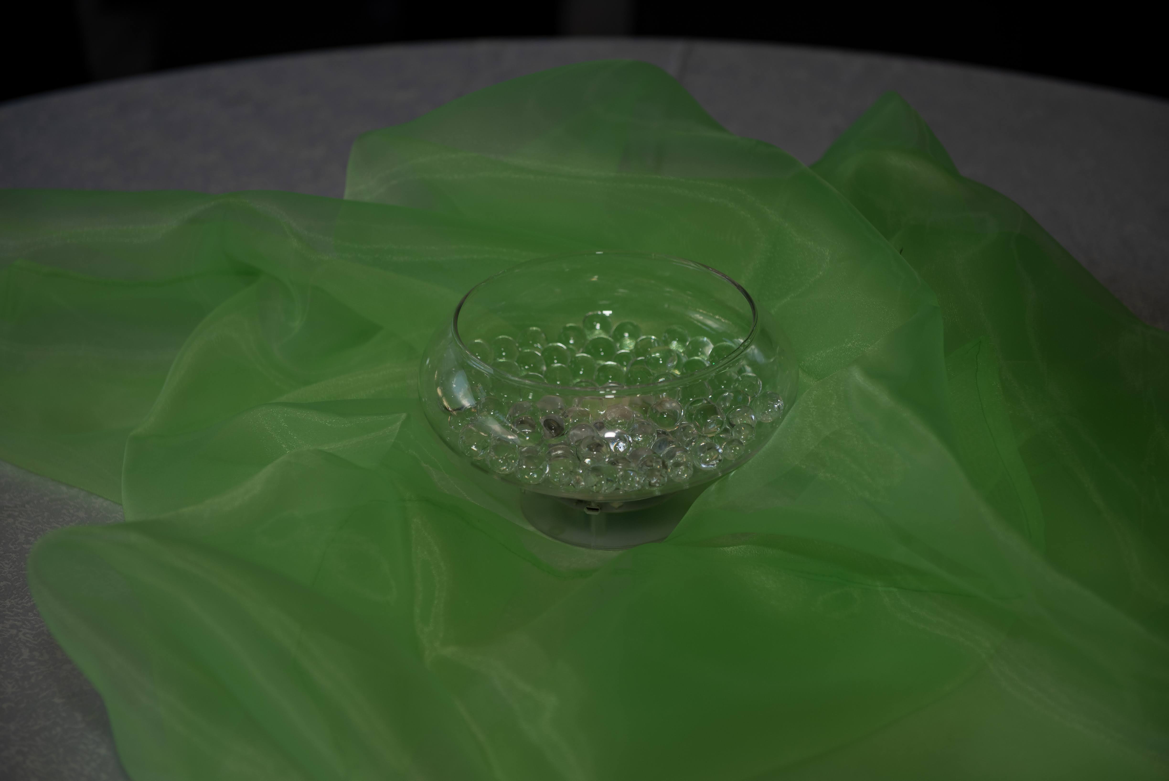 Glass bowl of gel beads set into folds of vivid green organza on a dark table