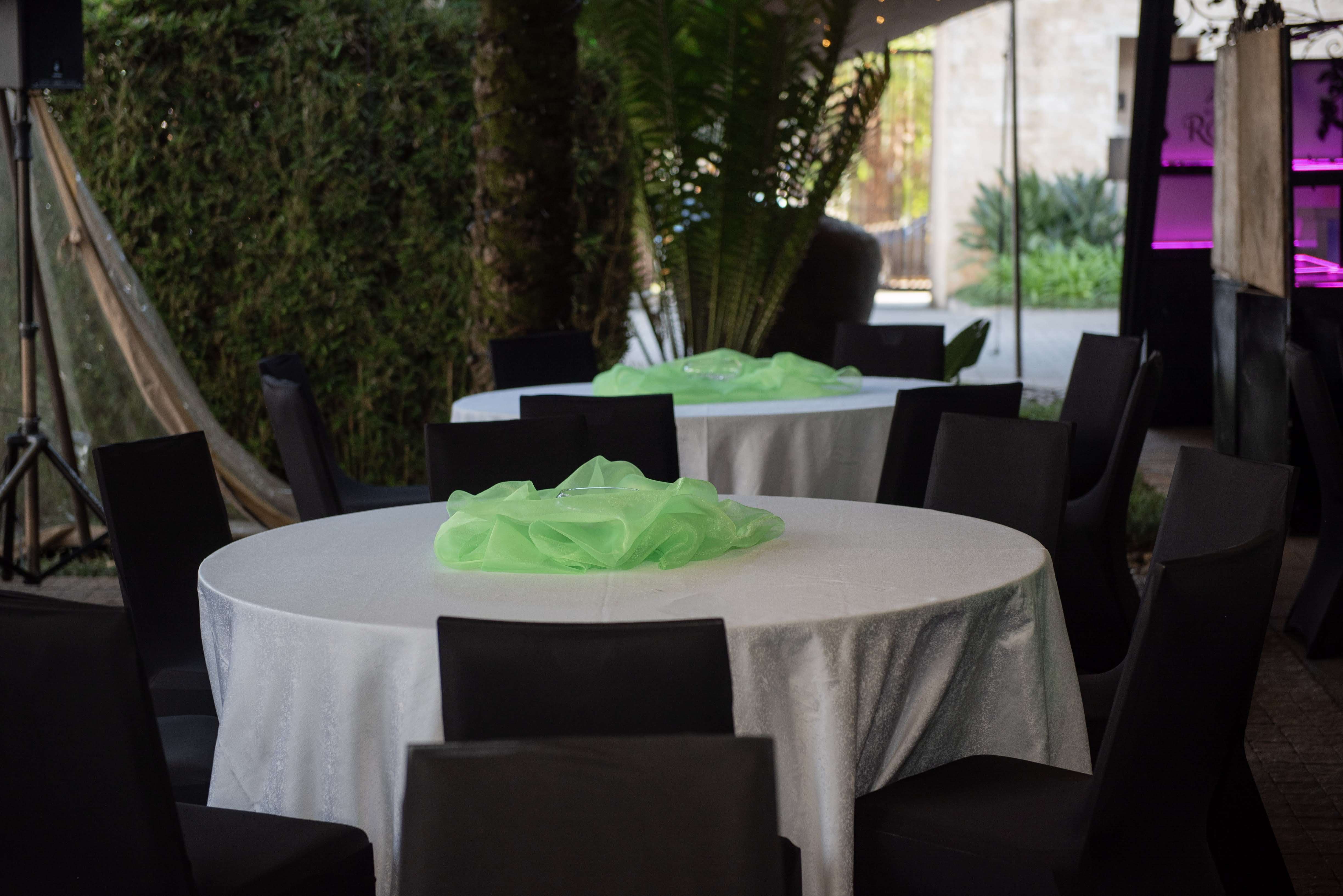 A fairy-lit stretch-tent dining room styled by Lilla Signatures, with green organza centrepieces on white tables beneath a canopy of warm string lights