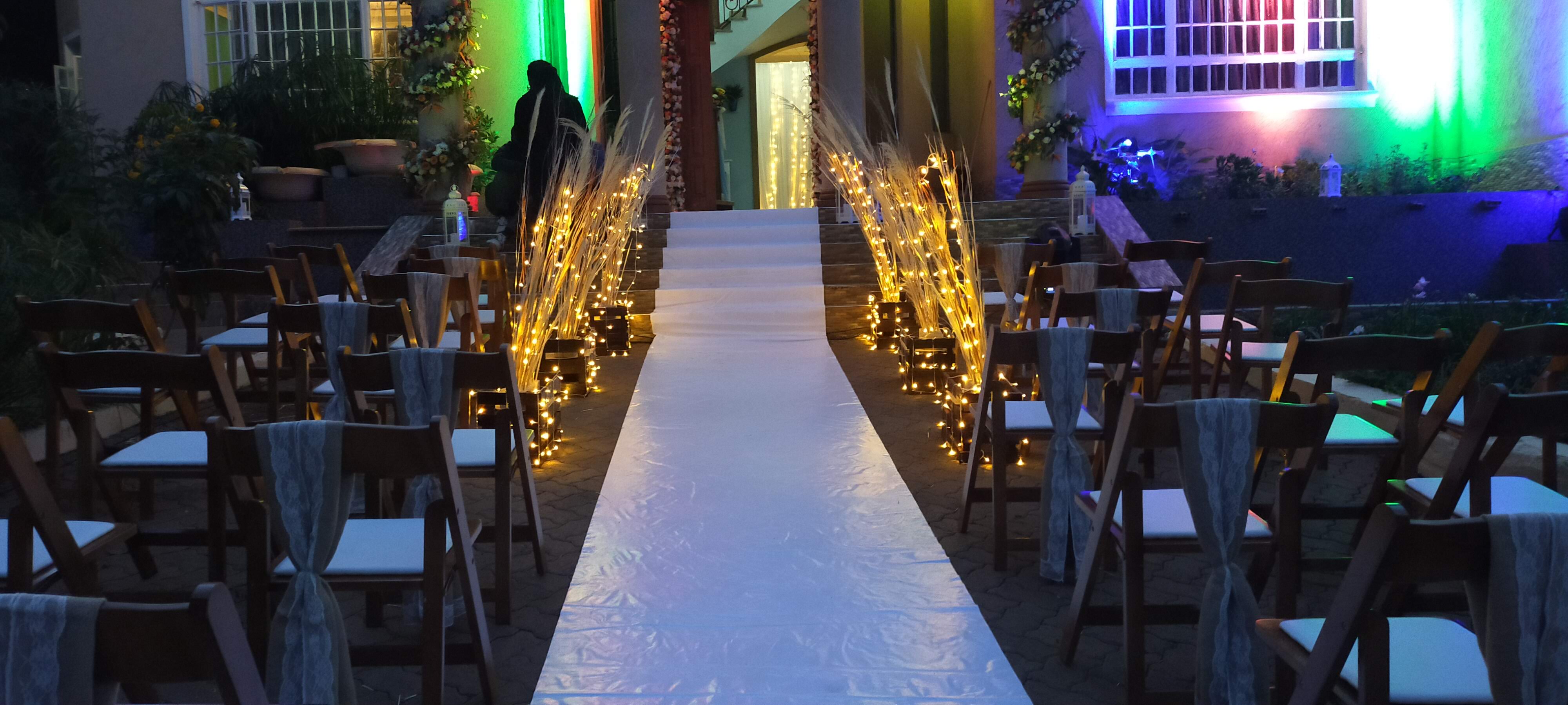 A candlelit garden aisle at dusk, lined with fairy-light bundles leading to a softly uplit doorway